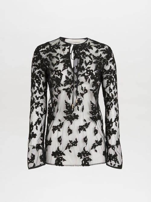 A long-sleeve, semi-sheer white Tosca Blouse Black Velvet featuring a black floral lace overlay and an abstract print keyhole tie neckline.