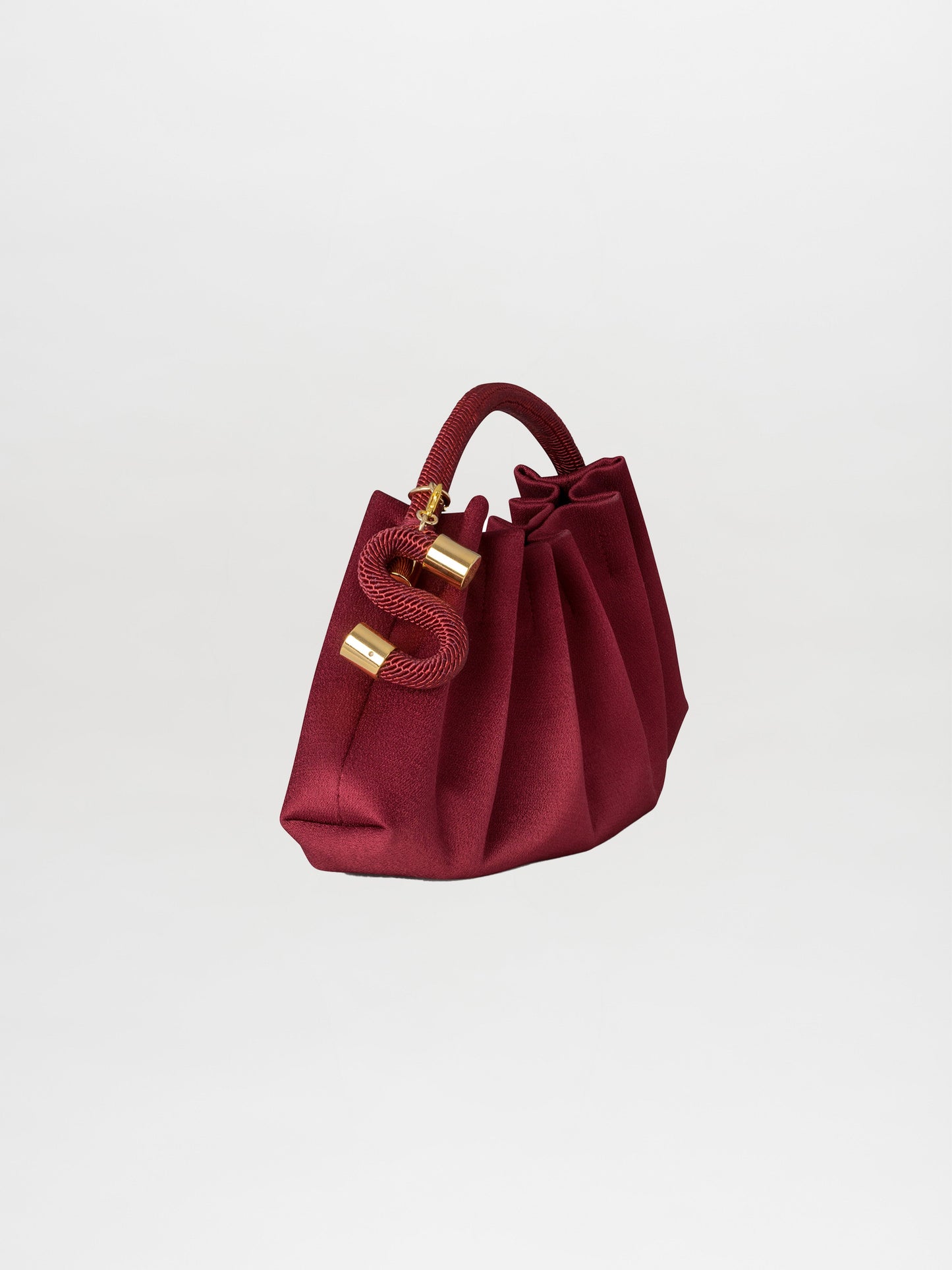 A burgundy Trapezius Clutch featuring a pleated design with a ruched texture, gold accents, and a red handle, set against a plain white background.