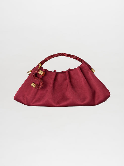 A burgundy Trapezius Clutch featuring a pleated design with a ruched texture, gold accents, and a red handle, set against a plain white background.