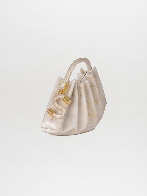 The Trapezius Clutch Cream, featuring a cream-colored pleated design with gold hardware and a looped rope handle, is elegantly showcased against a plain background.