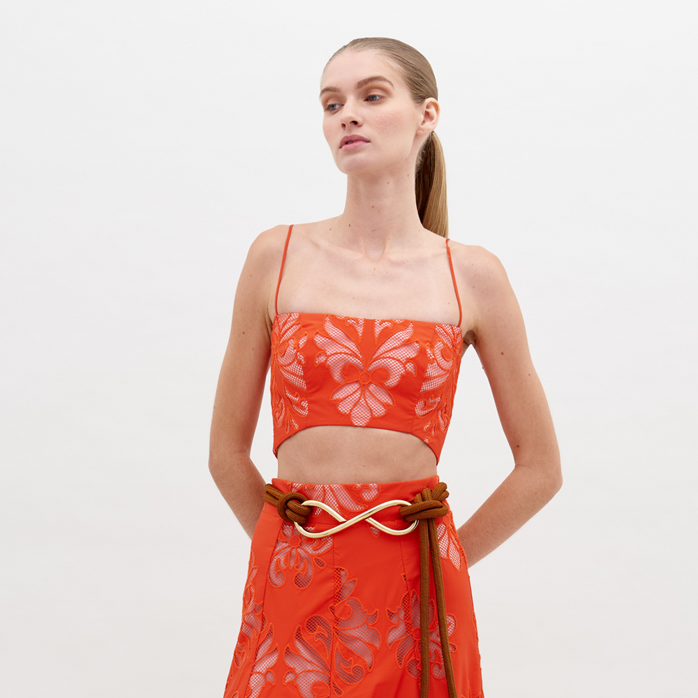 A person with long hair tied back wears an orange patterned Trini Top Rouge Embroidery and matching pants, standing against a plain background; keep an eye out for pre-order details, shipping by date scheduled for November 15th, 2024.