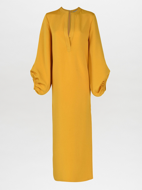 The Monferrato Tunic Amber is a long, mustard yellow dress with a high neckline and romantic balloon sleeves gathered at the wrists, featuring a small V-cut at the front. Perfect for Resort 2023, this amber-hued crepe tunic adds an elegant touch to your vacation wardrobe.