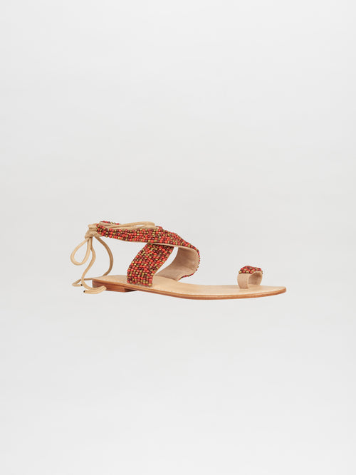 Introducing the Turin Sandal Red, a flat sandal perfect for summer adventures. It features red and beige bead embellishments and stylish ankle ties on a white background. Get ready to step out in style when you order this must-have product today!