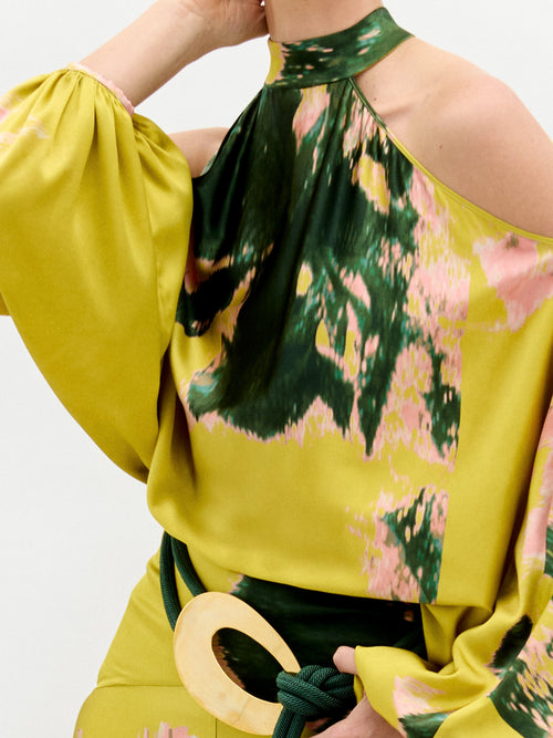 A person wearing the Valeria Dress, a long, colorful garment featuring a green and pink pattern, poses against a plain white background.