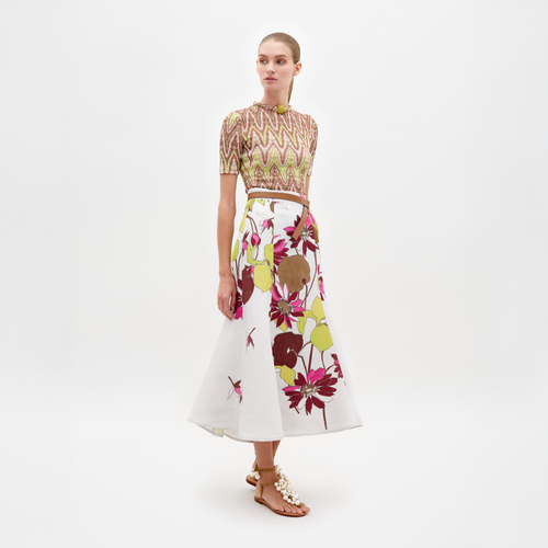 A woman is wearing the Varinia Tshirt Zigzag Neon and a floral skirt, showcasing her fitted silhouette as she looks to her left against a plain background.