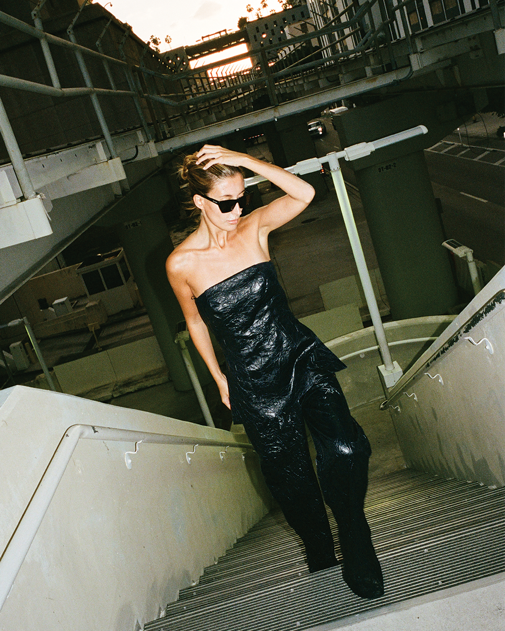 Person in a black strapless outfit standing on an industrial staircase.