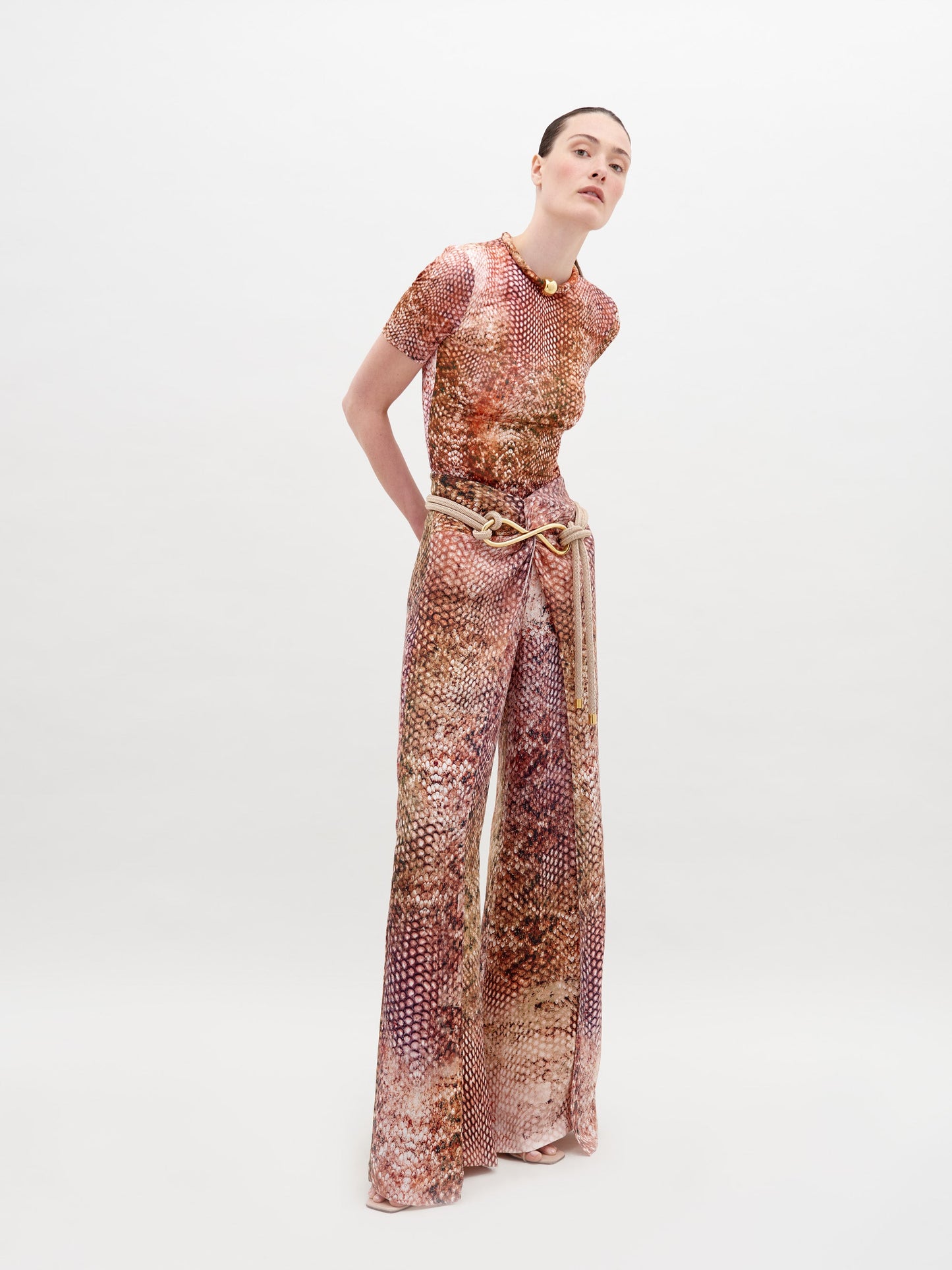 Person wearing a snakeskin-patterned outfit, consisting of a short-sleeve top and high-waisted, wide-leg Canturipe Pant Peach Animal Print, standing against a plain white background. This chic ensemble is available for pre-order and will ship by November 15th, 2024.