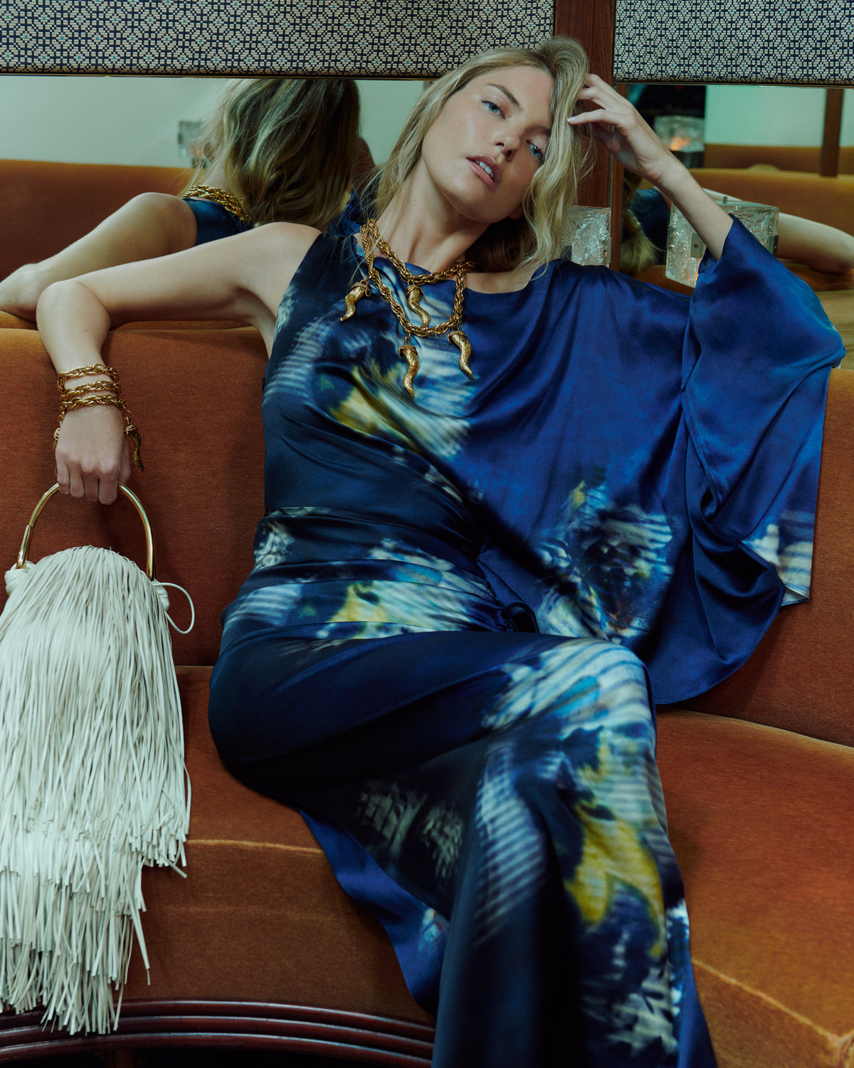 Woman in a blue dress sitting on an orange couch holding a white handbag.