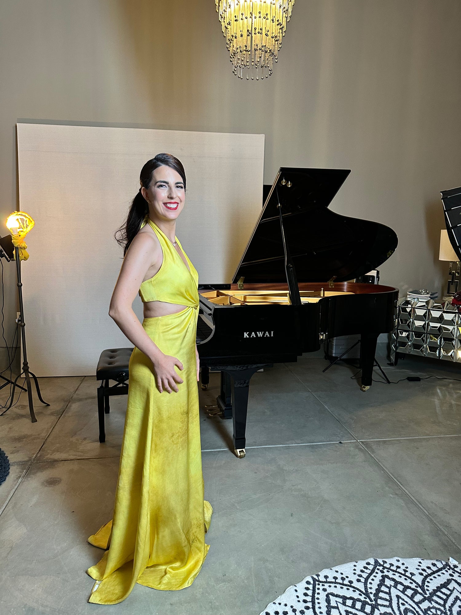 A woman in a yellow dress stands by a black grand piano in a room with modern decor.