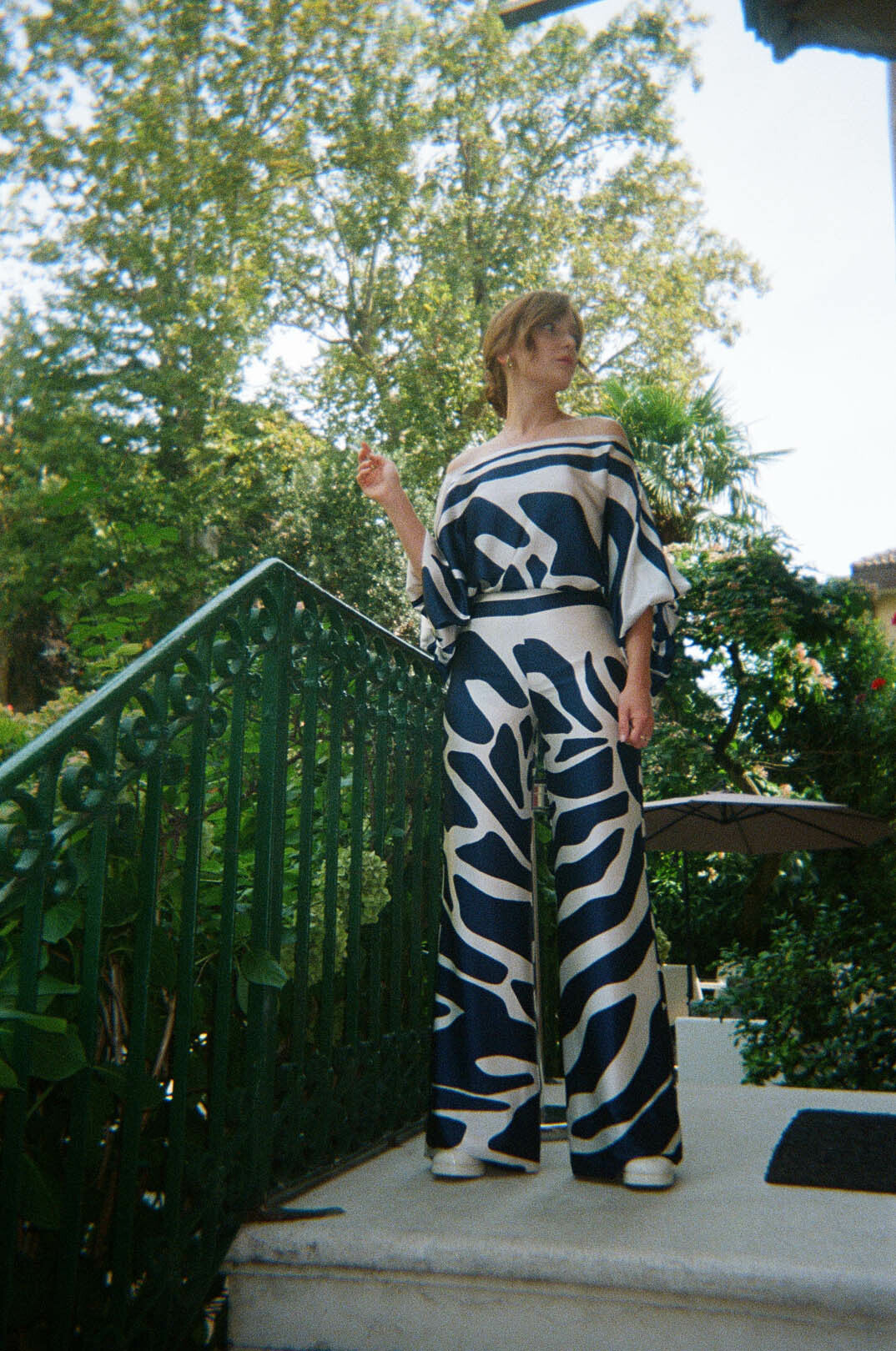 Person wearing a matching patterned top and pants stands on outdoor stairs, surrounded by greenery.