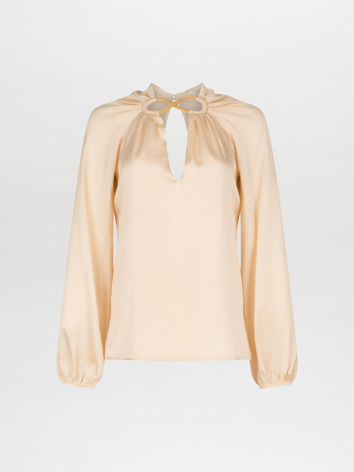 A Ximena Blouse Beige with a ruffled neckline and metallic detailing.