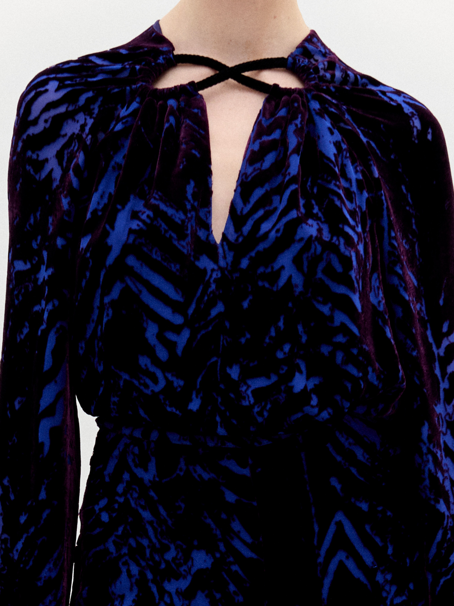 A person stands against a plain background wearing the Ximena Blouse in color eggplant velvet