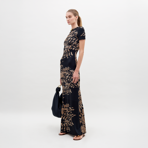 A woman stands against a plain white background wearing the Yara Dress Black Abstract Animal Print. She is holding a black bag and has her hair tied back in a low ponytail. Pre-order today for delivery by ship by date, November 15th, 2024.