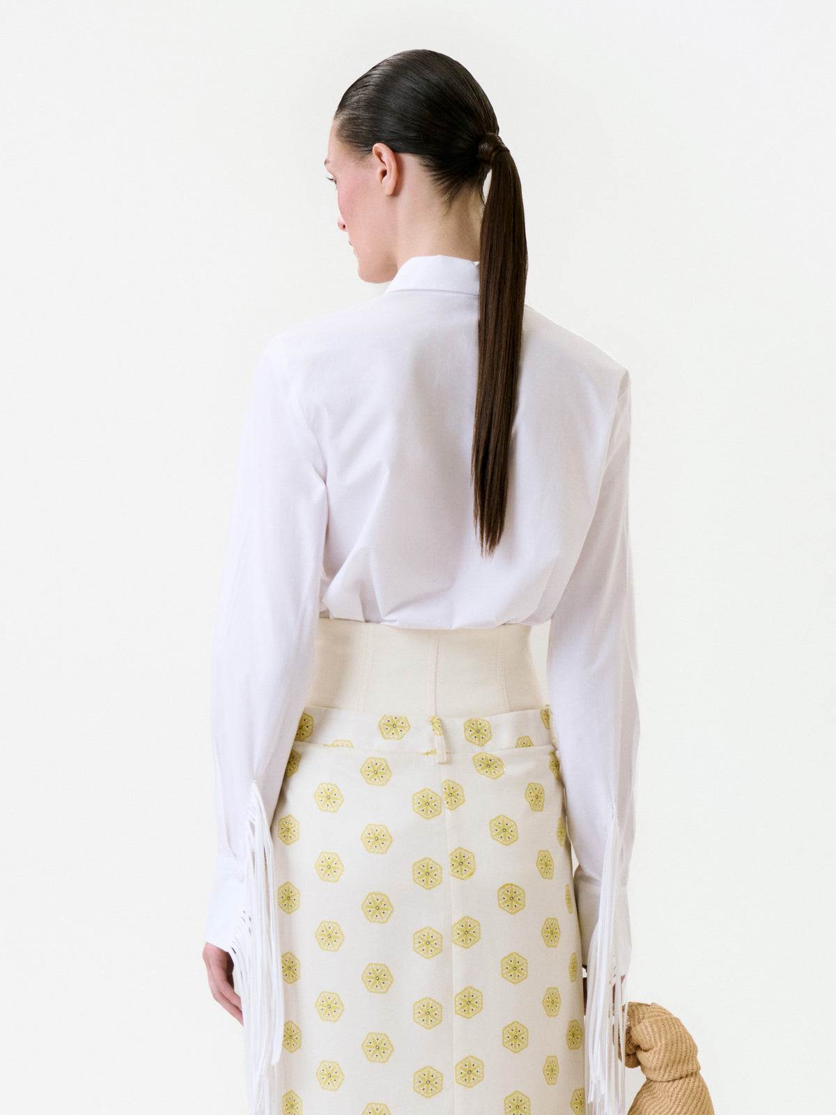 Back view of a person wearing a white Yemi Shirt with a collar and fringed cuffs, paired with a high-waisted patterned skirt.
