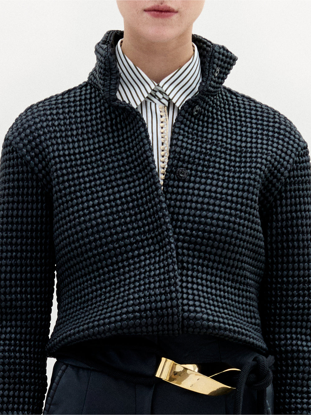 A person wearing the Zalta Jacket in color Black with a golden belt on a white background.