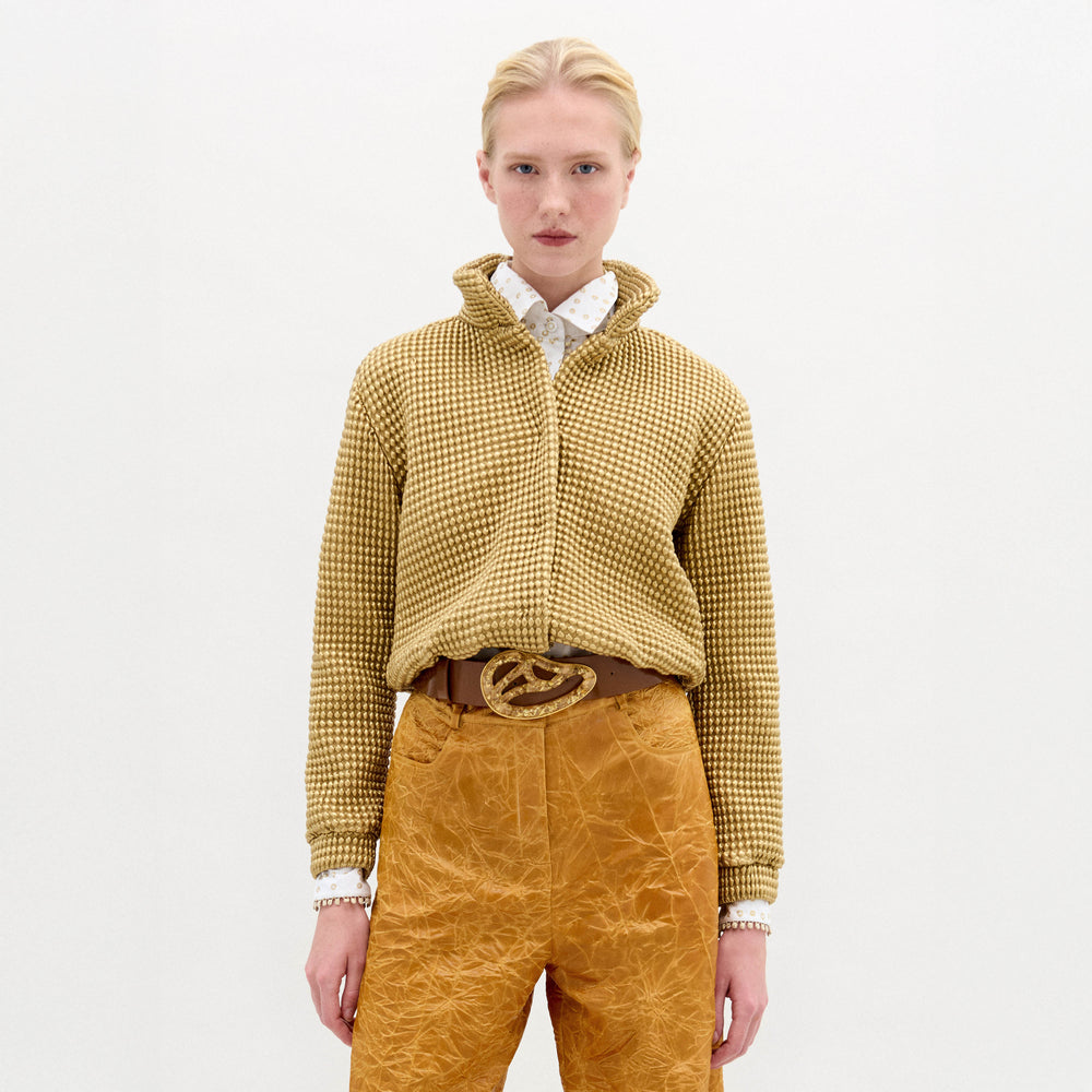 A woman wears the Zalta jacket, a brown sweater with an oversized fit, paired with gold pants.