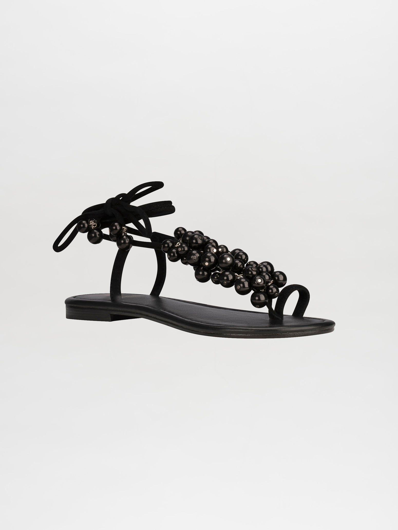 Introducing the Zaira Sandals Black: a sleek flat sandal featuring a black bead embellishment on the straps and a bow tie closure at the back, available for pre-order and set to ship by February 15th, 2025.