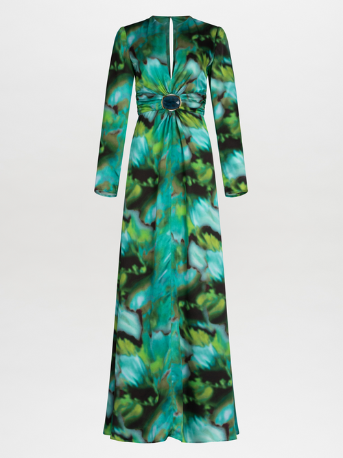 A person wearing the Zarina Dress Juniper Green, made of 100% silk, featuring a green and blue abstract multicolor print with a deep neckline and a central decorative brooch.