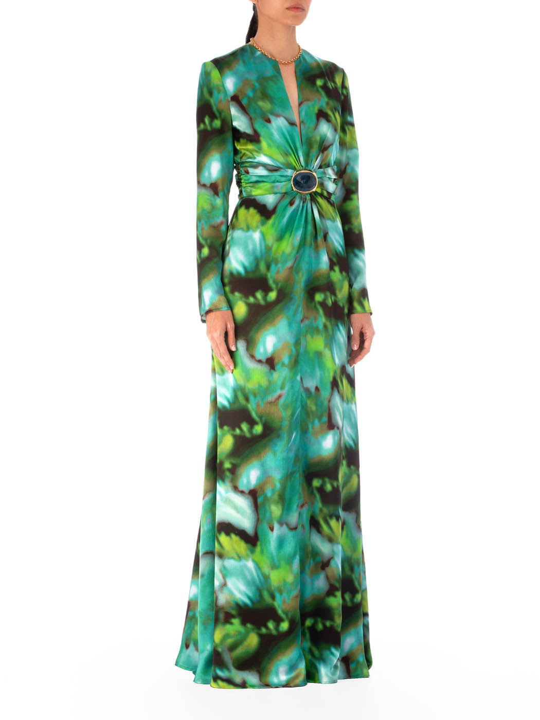 A person wearing the Zarina Dress Juniper Green, made of 100% silk, featuring a green and blue abstract multicolor print with a deep neckline and a central decorative brooch.