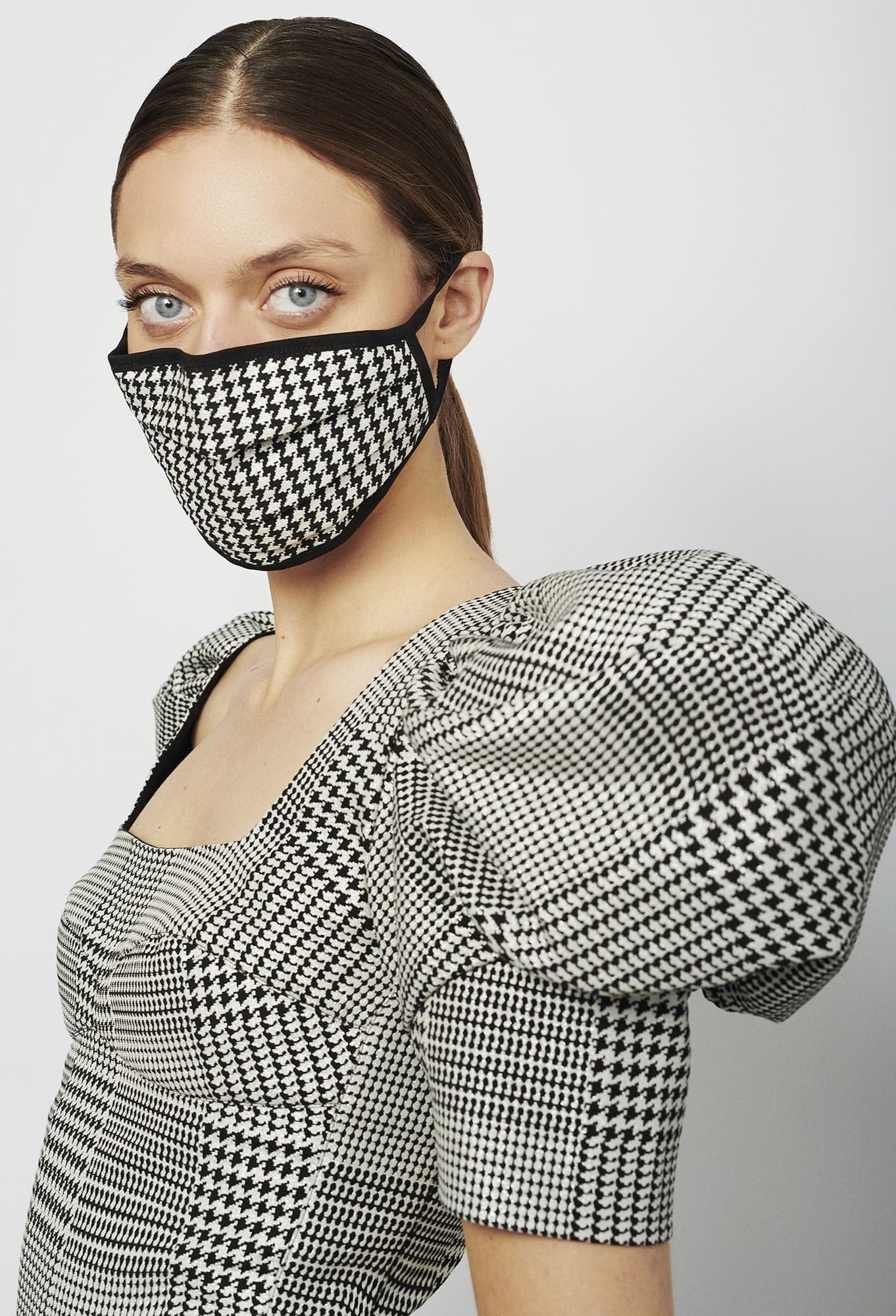 A person wearing a houndstooth-patterned face mask and dress with puffed sleeves.