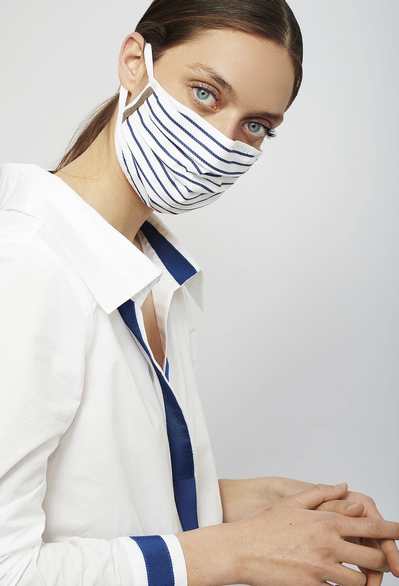 Person wearing a white shirt and a striped face mask, looking at the camera against a plain background.