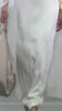 The supermodel Hillary Rhoda walking the runway wearing  the Kalina Dress, a floor-length, white sheer gown featuring a flowing cape sleeve and high neckline. Her hair is styled back as she gazes slightly to the side.