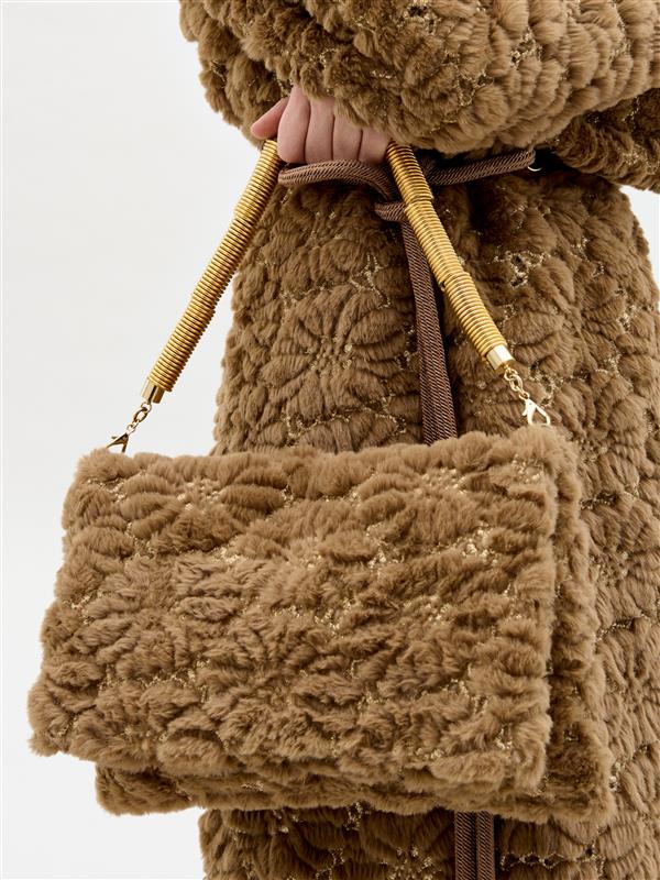 Brown textured handbag held by a person wearing a matching coat against a white background