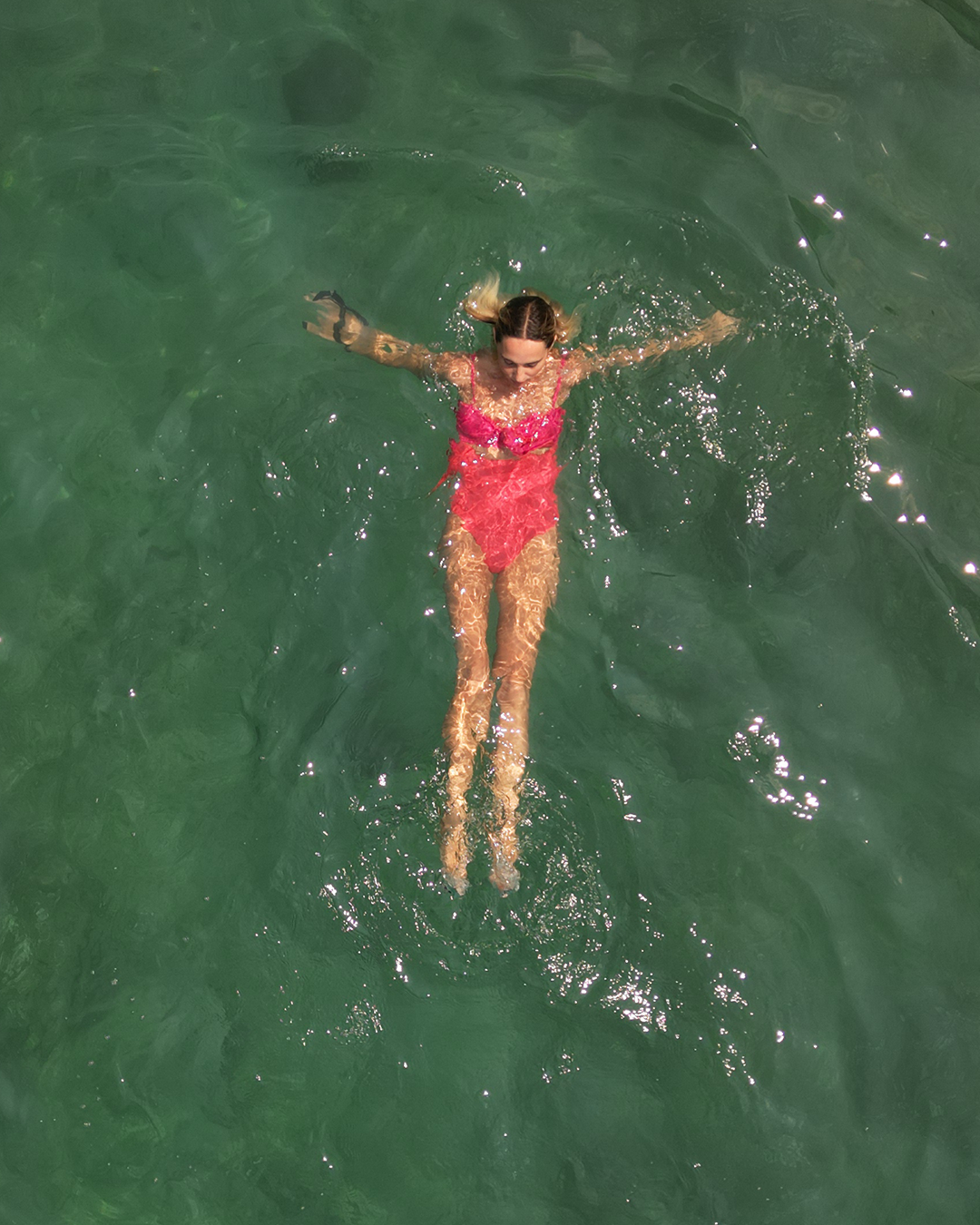 Person floating on their back in clear green water, wearing a pink swimsuit.