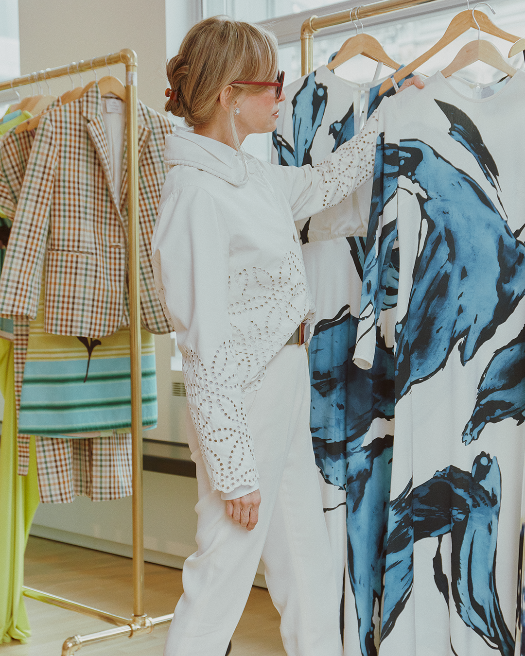 A person wearing a white outfit examines a garment with a blue and black abstract design on a rack.