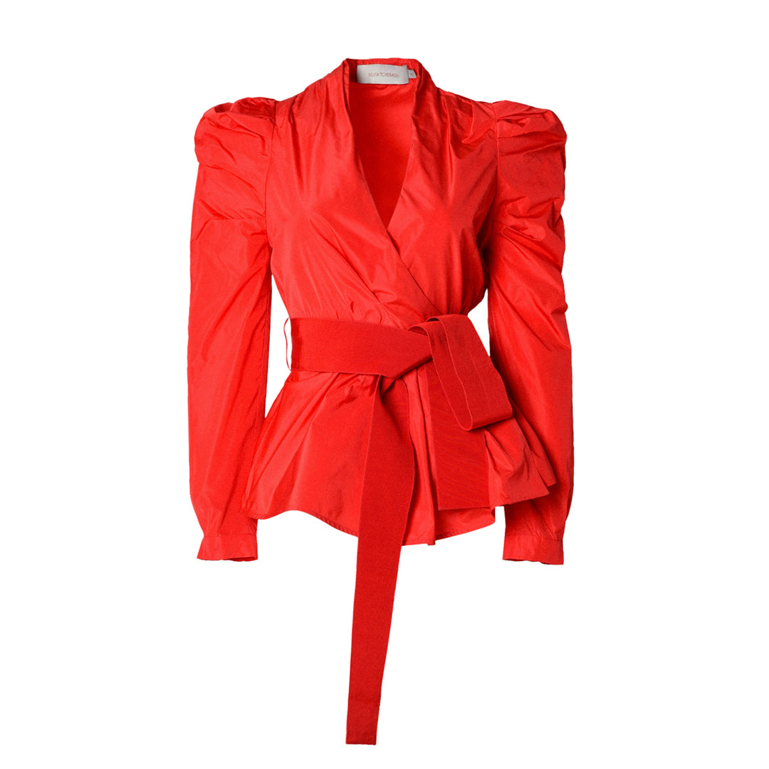 The Agnes Shirt Red is a vibrant scarlet women's blouse featuring puffed shoulders, a tailored waist, and a wide belt tied at the front.