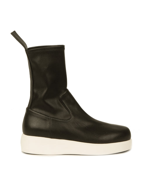 A black mid-calf Baia Boots Black with a white sole, side view. The boot, crafted from soft stretch calf leather, features a pull tab at the top rear and a sleek, smooth upper.