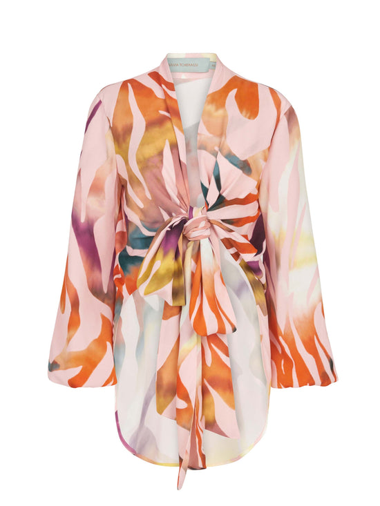 The Honey Blouse Blush Prismatic is a long-sleeve top with a vibrant abstract zebra print in pink, orange, yellow, and white. It features a front tie knot design and a flowy silhouette.