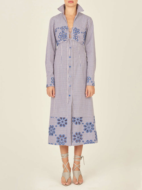 The Ganzoni Dress Navy Floral is a long-sleeve, button-down dress with a collar, featuring a blue and white checkered pattern and blue floral designs. This item is part of our Final Sale and is not eligible for return or exchange.