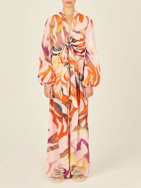 The sentence can be rewritten as: "Ovada Pant Blush Prismatic high-waisted trousers are made from crepe de viscose, showcasing a vibrant abstract pattern in shades of red, orange, and pink on a white background.