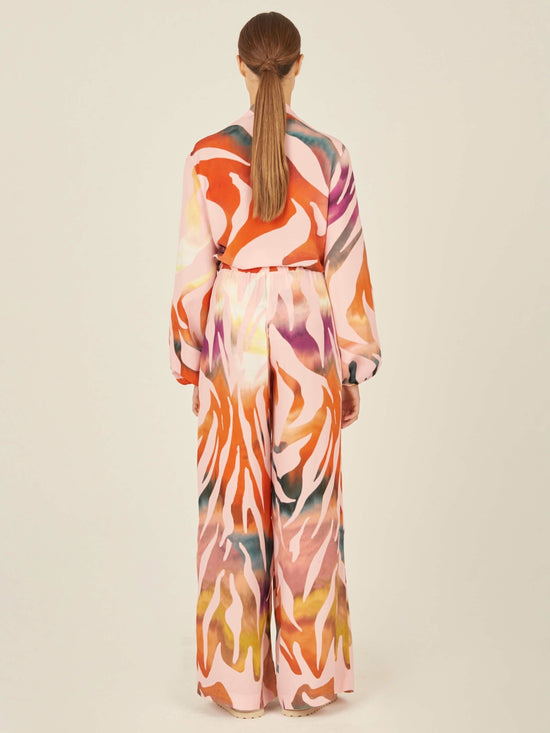 The sentence can be rewritten as: "Ovada Pant Blush Prismatic high-waisted trousers are made from crepe de viscose, showcasing a vibrant abstract pattern in shades of red, orange, and pink on a white background.