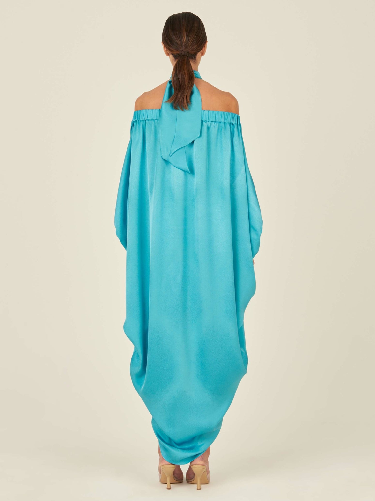 A Jacqueline Kaftan Turquoise with a halter neck and draped design, made from turquoise crepe fabric and featuring loose, flowing material.