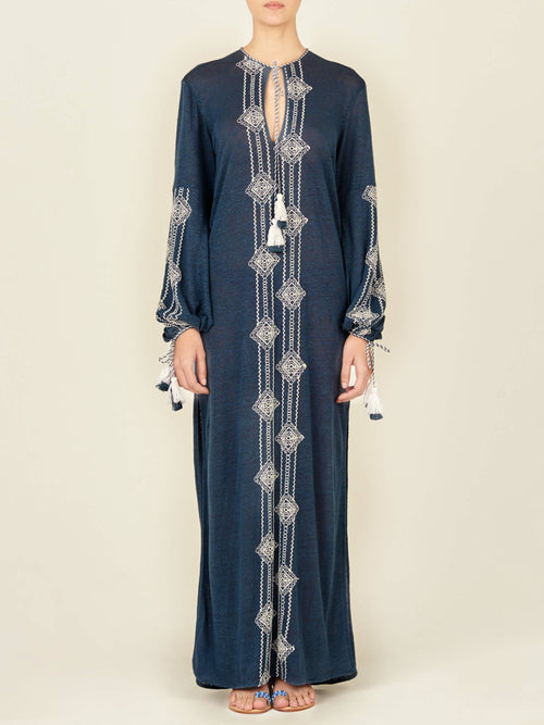 A navy blue, long-sleeved Mayfair Tunic Navy Embroidered with a V-neckline featuring white geometric embroidery down the front and on the sleeves, finished with tasseled ties at the cuffs.