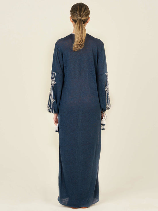 A navy blue, long-sleeved Mayfair Tunic Navy Embroidered with a V-neckline featuring white geometric embroidery down the front and on the sleeves, finished with tasseled ties at the cuffs.