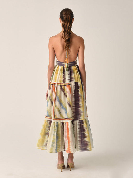 The Valerie Dress Multi Hazy Stripe is a sleeveless halter-neck midi dress featuring a vibrant multi hazy stripe tie-dye pattern and a charming tiered skirt.