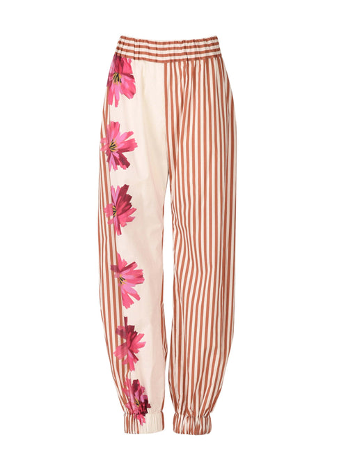 The Chilean Pant Magenta Floral Brushstroke Stripes features light-colored fabric with brown vertical stripes and a magenta floral design on one side. It also comes with an elastic waistband and cuffs for casual luxury.