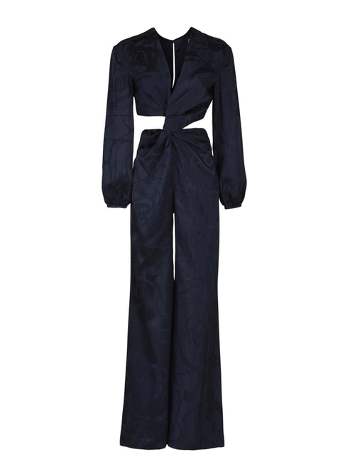 The Joely Jumpsuit Navy Jacquard, a black long-sleeve piece from the Resort 2023 collection, features a twisted front design, cutout at the waist, and wide-leg trousers.