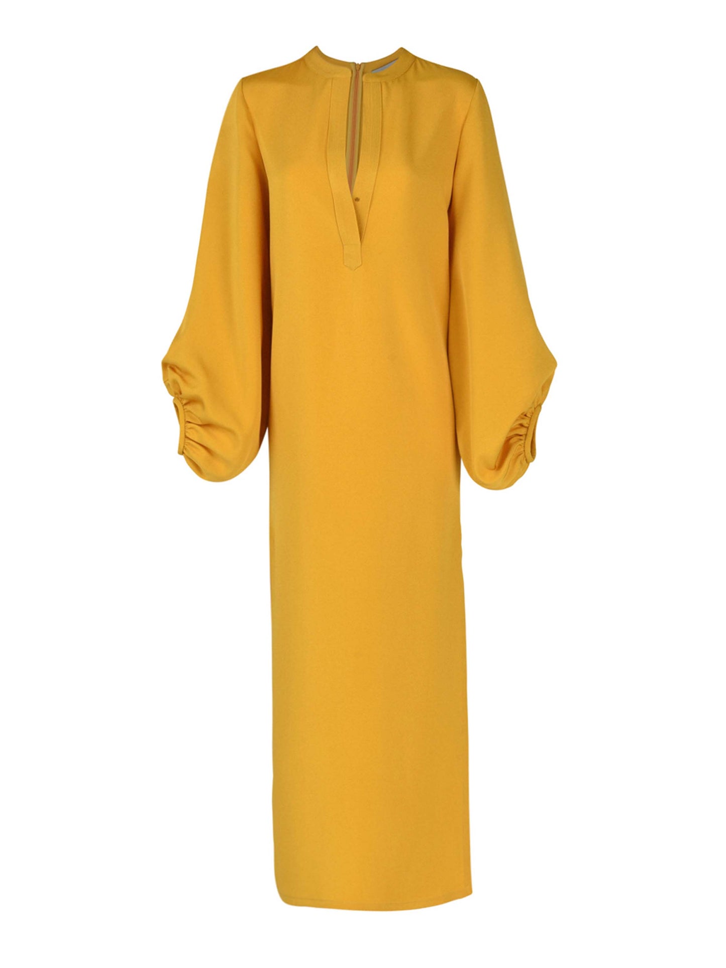 The Monferrato Tunic Amber is a long, mustard yellow dress with a high neckline and romantic balloon sleeves gathered at the wrists, featuring a small V-cut at the front. Perfect for Resort 2023, this amber-hued crepe tunic adds an elegant touch to your vacation wardrobe.