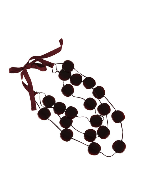 The Olivia Necklace Burgundy is a string of black round acrylic beads connected by a black thread with a red ribbon tied at one end, isolated on a white background.