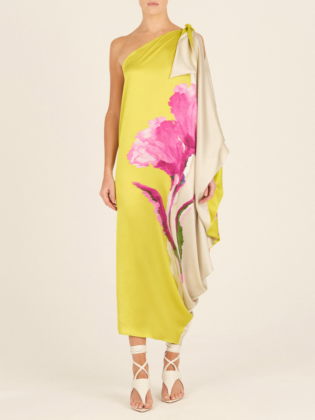 The Crema Tunic Chartreuse Beige Floral is a one-shoulder, asymmetrical silk tunic adorned with large pink floral prints and featuring a draped sleeve.