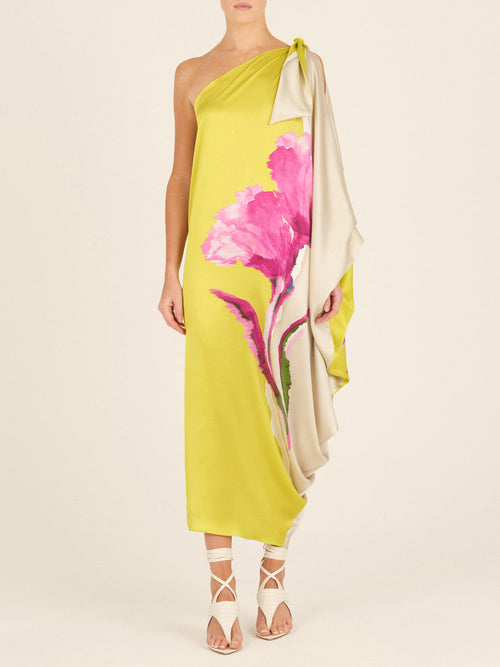 The Crema Tunic Chartreuse Beige Floral is a one-shoulder, asymmetrical silk tunic adorned with large pink floral prints and featuring a draped sleeve.