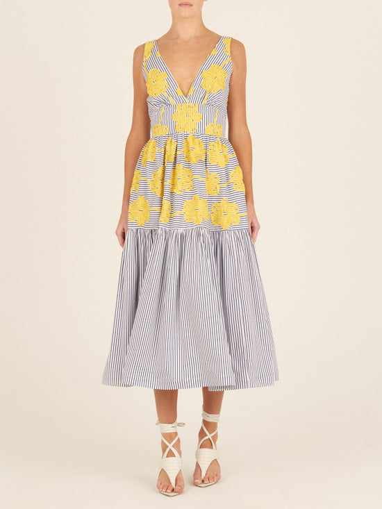 The Eugene Dress, adorned with yellow floral embroidery, showcases a sleeveless design with blue and white vertical stripes, a V-neckline, and a long-tiered skirt.