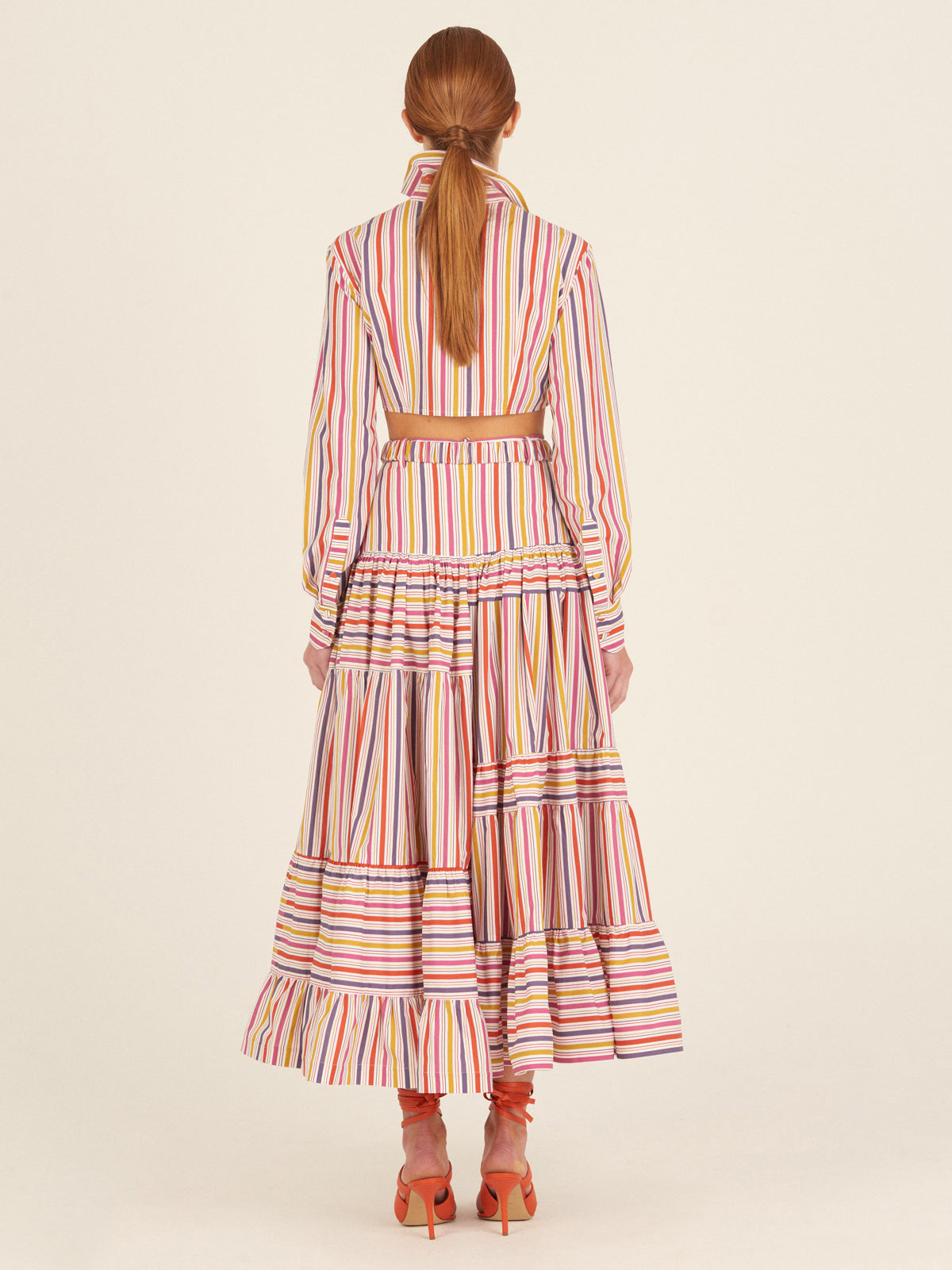 Marcel Blouse Golden Magenta Stripes in cropped style, featuring a twist front detail and multicolored gold magenta striped fabric, complete with buttoned cuffs.