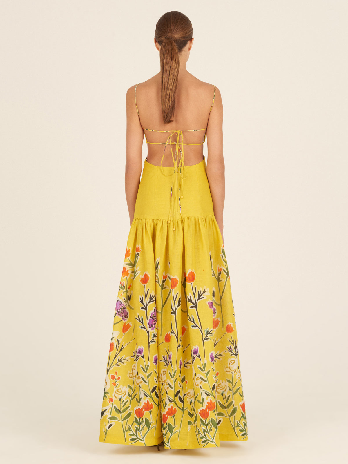 The Shannon Dress Golden Wallflowers is a yellow sleeveless maxi dress with thin straps, boasting a fitted bodice and a flared skirt adorned with colorful floral embroidery near the hem, making it perfect as a vacation maxi dress.