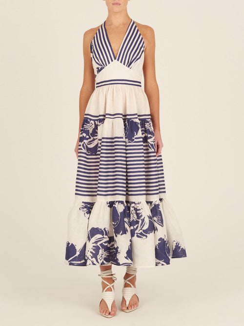 The Valerie Dress Azure Floral Stripes is a charming addition to your Spring 2023 wardrobe, featuring a sleeveless, halter-neck design with azure floral stripes and blue floral prints on the skirt and hemline.