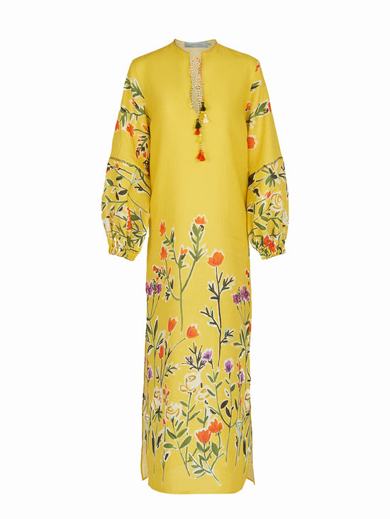 The Cala Tunic Golden Wallflowers is a long yellow dress adorned with a multicolor floral pattern of golden wallflowers, featuring wide sleeves and a tassel detail at the neckline, reminiscent of kaftan-style.